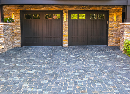 two wooden garage doors with windows on a cobblestone driveway 